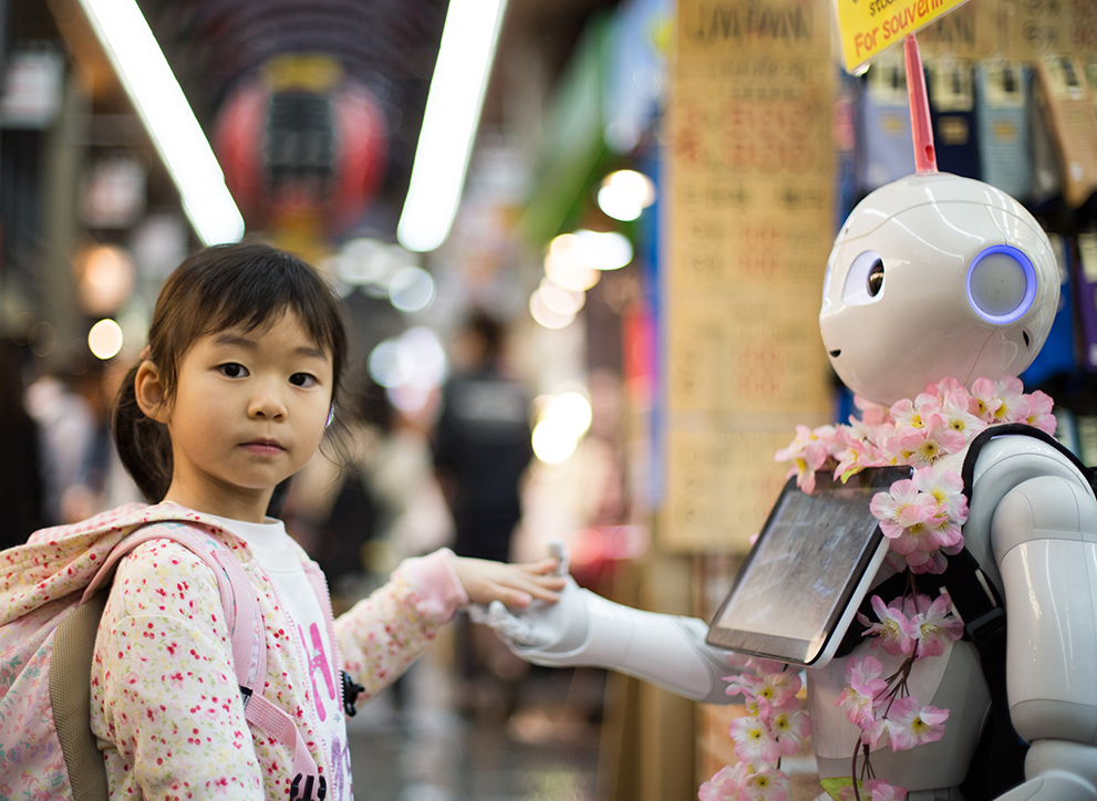 A young girl holds the hand of a robot on display at the Kuromon Market in Osaka. Photo by Andy Kelly on Unsplash.
